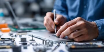 Technician repairing a MacBook with tools and components.