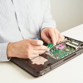 Man repairs computer. A service engineer in a shirt repairs a laptop, at a white Desk against a white wall, close up